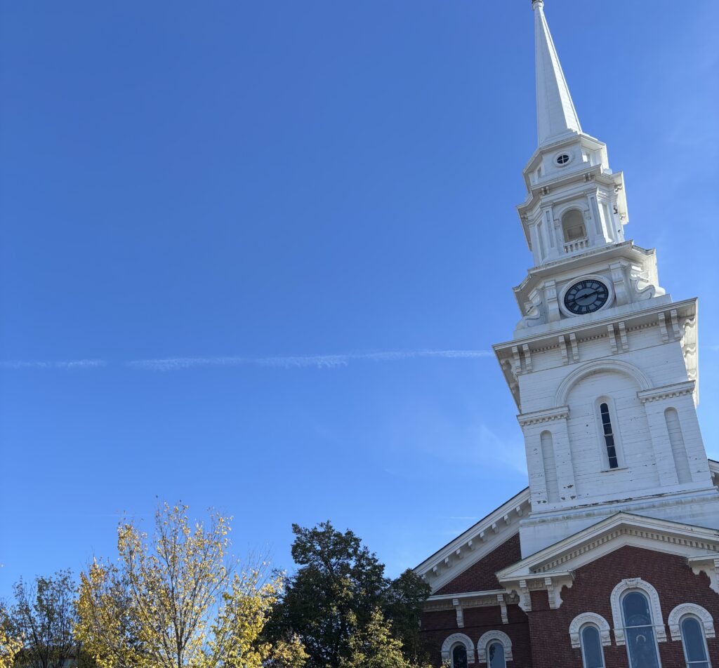 The steeple of North Church on Congress Street in Portsmouth, New Hampshire against a blue sky with a few trees below.
